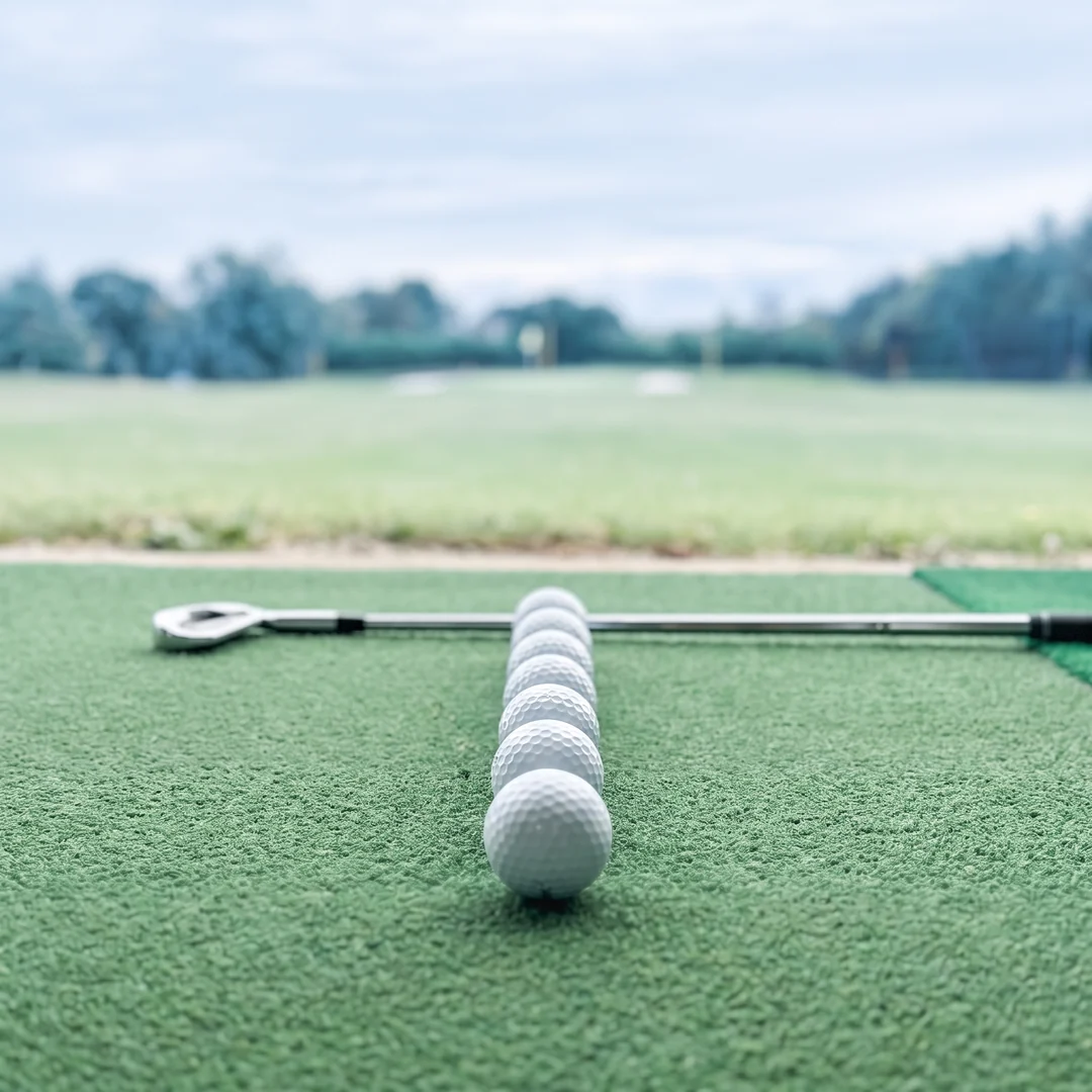 A row of golf balls and an iron on a driving range mat